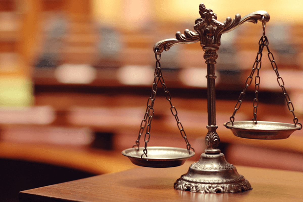 Bilancia della giustizia in ottone su un banco di legno, davanti ai banchi dell'aula