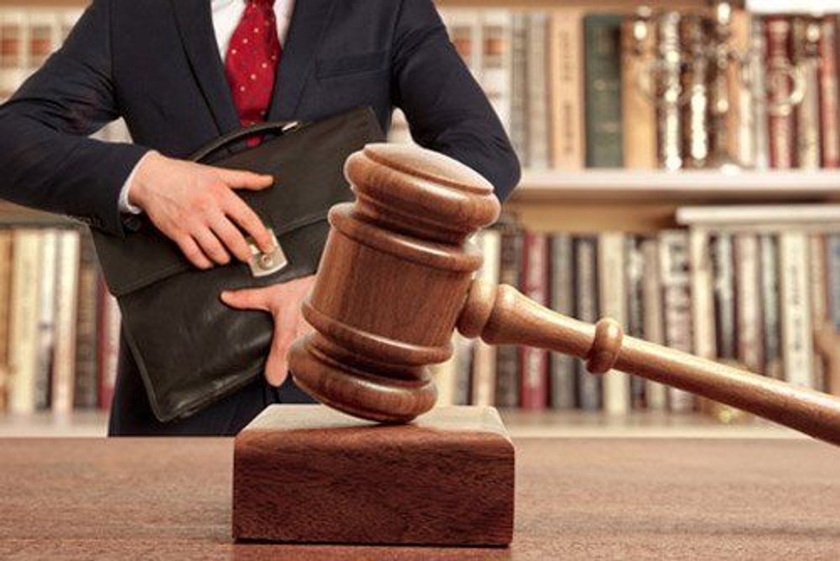 Martelletto del giudice davanti a una libreria, accanto a una borsa da avvocato